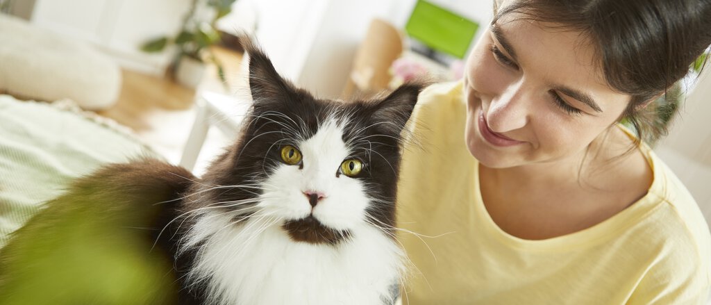 Frau liegt mit ihrer Katze im Bett und lächelt