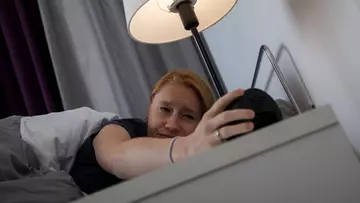 Frau schaut völlig müde mitten in der Nacht auf einen Wecker. (Bild: Christin Klose)