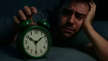 Mann schaut völlig müde mitten in der Nacht auf einen Wecker. (LVM Versicherung / KI-generiertes Bild)