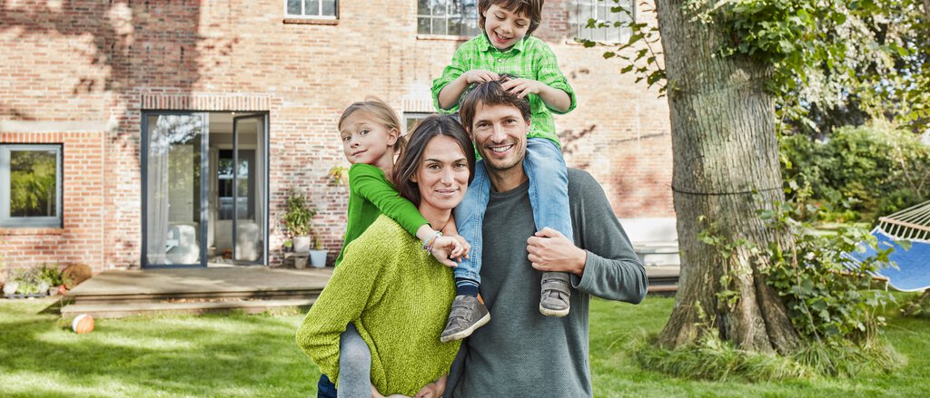 Familie mit zwei Kindern im Garten hinter dem Haus spielen sorgenfrei danke der Wohngebäudeversicherung der LVM