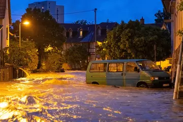 Vor der Skyline der Stad Frankfurt am Main steht ein Fahrzeug im Hochwasser. 