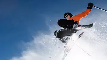 Skifahrer fliegt im Pulverschnee über die Piste.