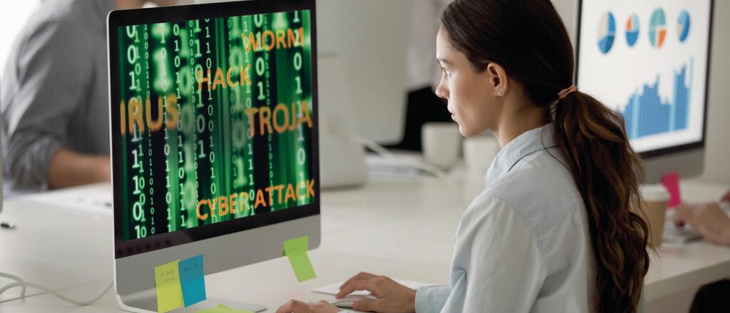 Cyberversicherung - Junge Frau im Großraumbüro vor Bildschirm