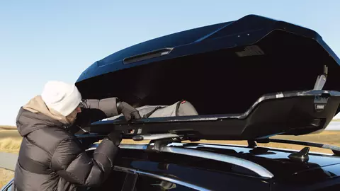 Frau holt etwas aus einer geöffneten Dachbox auf einem Autodach