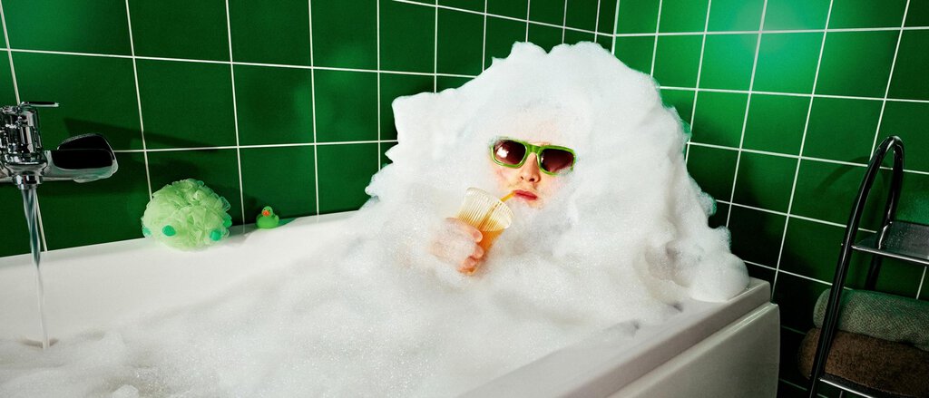 Ein junger Mann steht vor einem überdimensionalen gelben Smiley vor einem grünen Hintergrund.