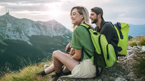 Ein junges Paar sitzt vor einem Bergpanorama und genießt sorglos den Urlaub. Die Reiserücktrittsversicherung der LVM ist mit im Gepäck.