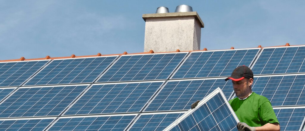 Photovoltaikversicherung Arbeiter verlegt Photovoltaikmodule auf Hausdach