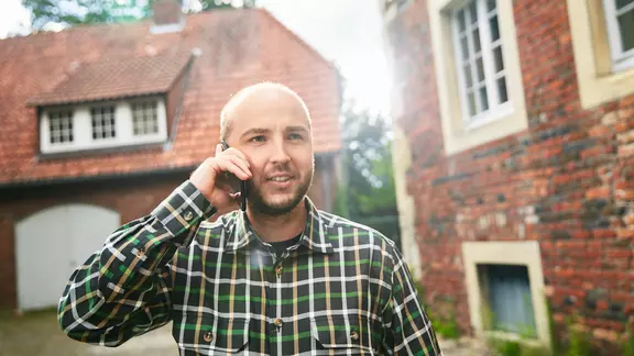 Mann am Telefon vor Haus