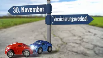 Zwei Modell-Autos beim Aufprall vor Schildern, die das Datum 30. November für den Versicherungswechsel zeigen. 