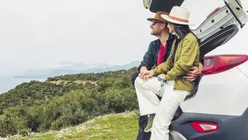 Ein Paar sitzt im Kofferraum ihres Mietwagens und blickt aufs Meer.  (Foto: picture alliance/imageBROKER/Evaldas Mikoliunas)