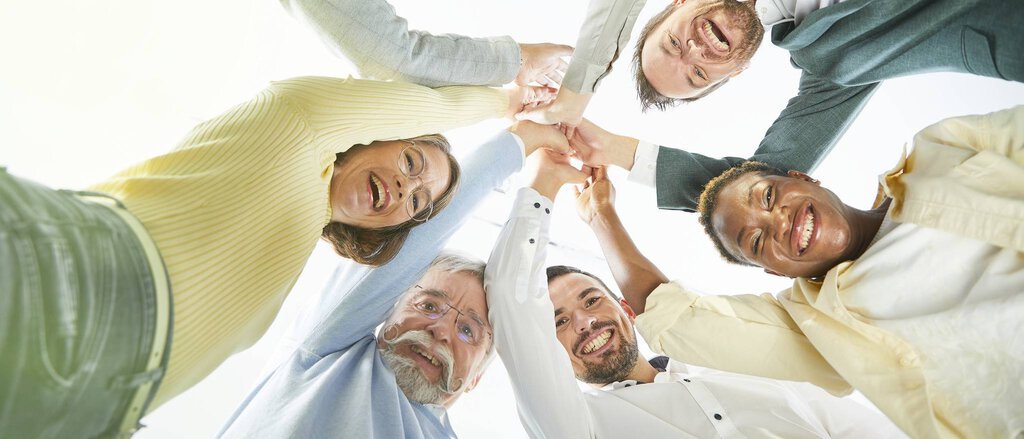 Vereinshaftpflichtversicherung Eine Gruppe von Personen hält sich gegenseitig an den Händen und lacht in die Kamera, dank der Vereinshaftpflichtversicherung.