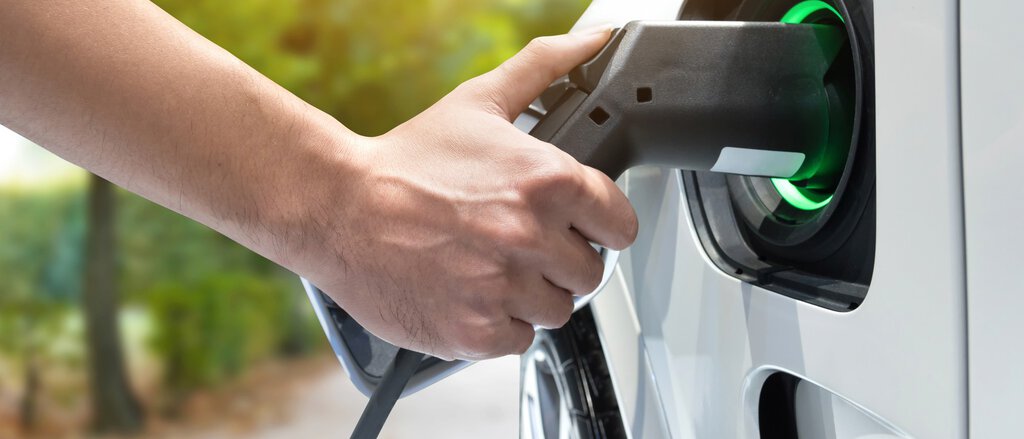 Eine Hand hält das Ladegerät für das E-Auto in die Ladevorrichtung am Auto. Dank der THG-Quote ist der Umstieg auf elektronische Fahrzeuge erleichtert.