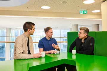Drei Männer sprechen miteinander, während sie Kaffee trinken.