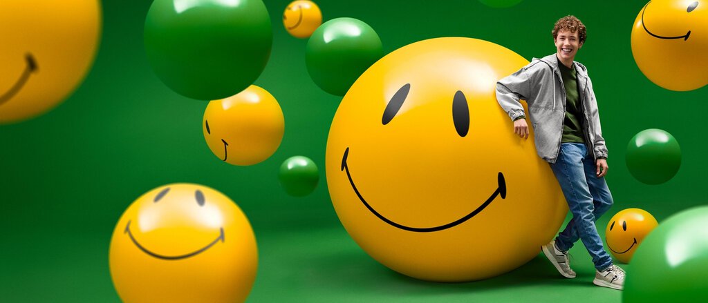Happy versichert? Wir kümmern uns darum! Humorvolles Bild: Ein junger Mann lehnt entspannt an einem überdimensionalen gelben Smiley vor einem grünen Hintergrund. Er ist froh darüber, dass die LVM alle Versicherungsangelegenheiten für ihn regelt.
