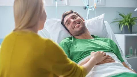 Junger Mann mit Reiserücktrittsversicherung wird von Freundin im Krankenhaus besucht