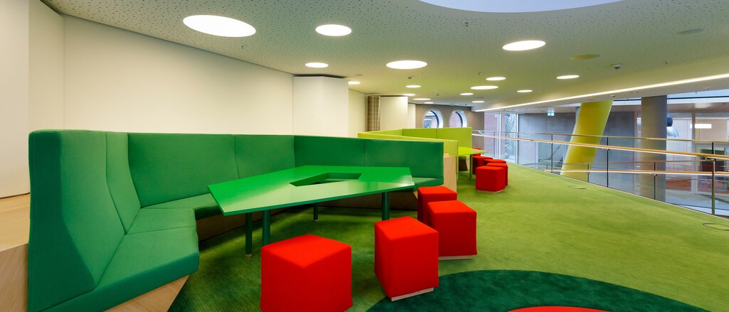 Procedure for objection report concerning human rights and the environment Räumlichkeiten der LVM, langes grünes Sofa, rote Hocker vor weißem Tisch, grüner Teppich