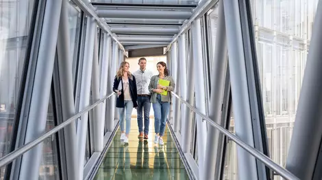 3 Personen laufen über die Glasbrücke der LVM-Zentrale