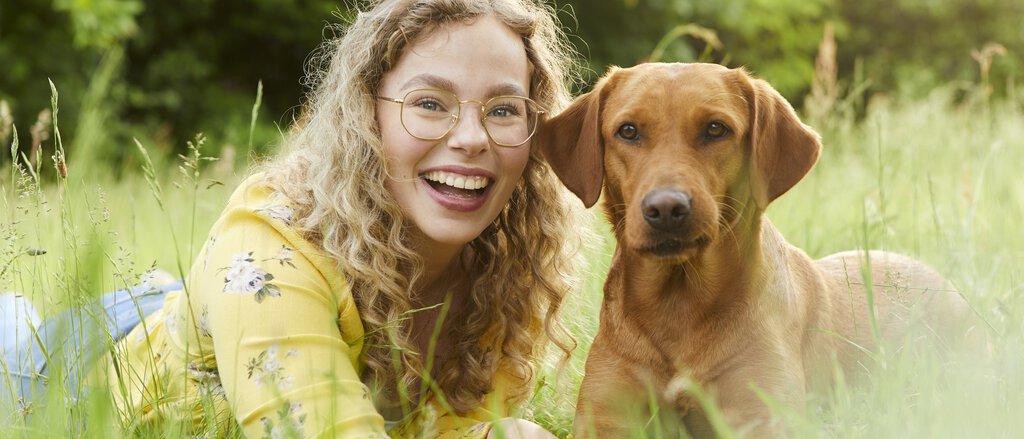 Frau mit Hund auf einer Wiese liegend