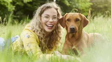 Eine junge, lächelnde Frau liegt mit ihrem Hund auf einer Wiese. Eine Tierkrankenversicherung bietet eine breite medizinische Versorgung für Vierbeiner. (Foto: LVM Versicherung)  