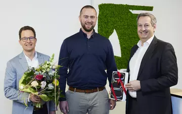 Ein LVM-Kunde bekommt einen Blumenstrauß und ein Geschenk von zwei LVM-Repräsentanten überreicht.