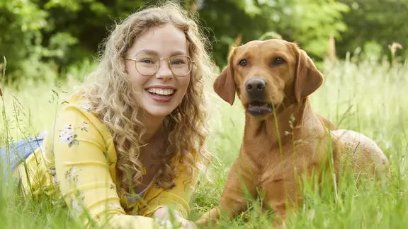Junge Frau mit Hund auf einer Wiese denkt über die Hundekrankenversicherung nach.