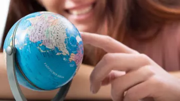 Eine junge Frau sitzt an einem Tisch und schaut auf einen kleinen Globus.