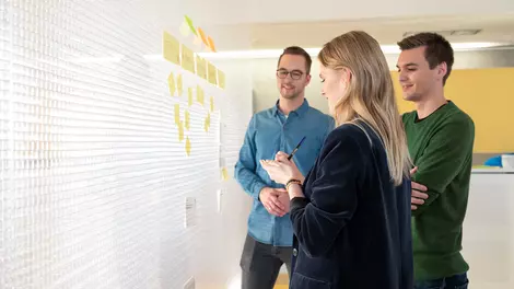 3 Personen stehen an einem Flipchart und diskutieren mit Post-Its